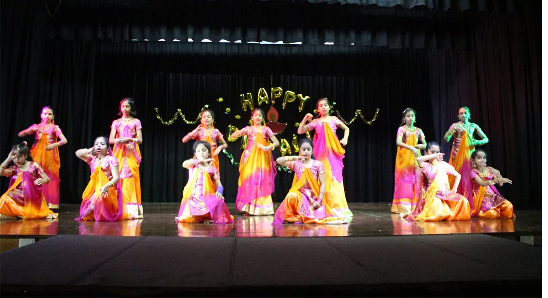 Students in orange and pink saris performing a traditional dance at a Diwali celebration